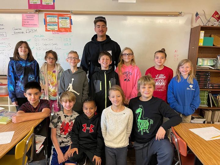 Ralph posing for photo with 4th grade students in classroom.